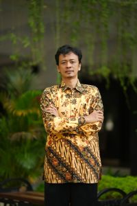 A man wearing batik with a greenery background