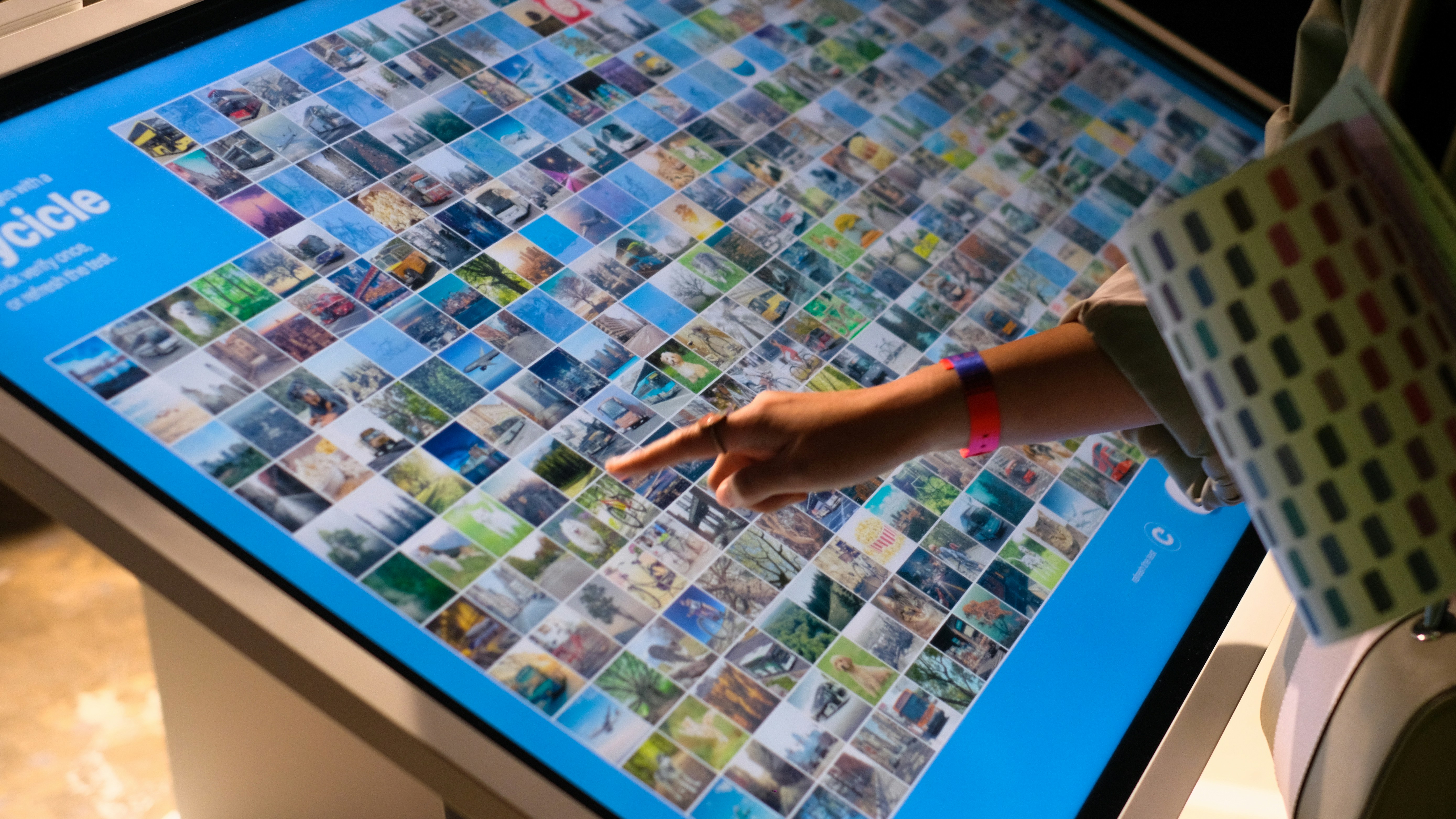 A person pointing at a large display of pictures on touchscreen