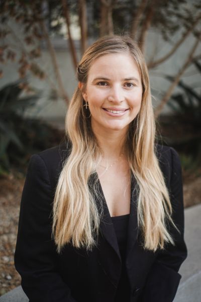 Kathryn Baragwanath, 2025 Paul Bourke Award winner smiles at the camera. She has long blonde hair and is wearing a black jacket.