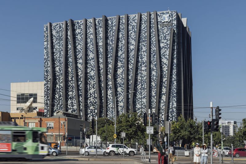 An image of The Spot building on the University of Melbourne's Parkville campus. There is a tram and some pedestrians in the foreground.
