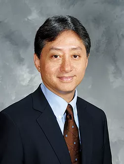 Head shot of a man in a suit smiling against a grey background