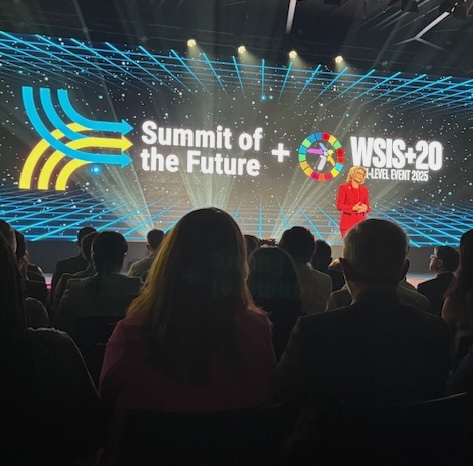 Large 'Summit of the Future' screen with crowd standing in front of and looking at.